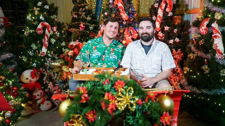 Nick and boyfriend sitting in sleigh with tray of food, in Christmas tree room, as seen on Hoarding for the Holidays, Season 1.
