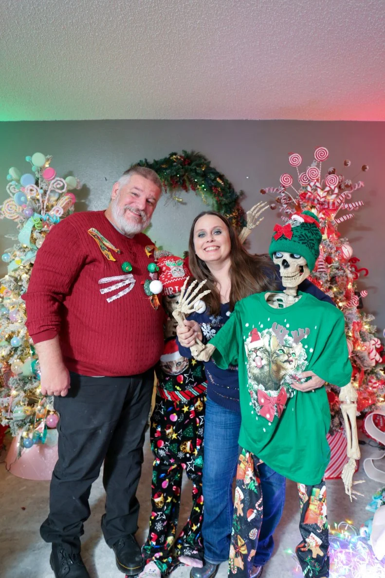 Christa and her fiancé posing for a picture while holding skeletons, as seen on Hoarding for the Holidays, Season 1.