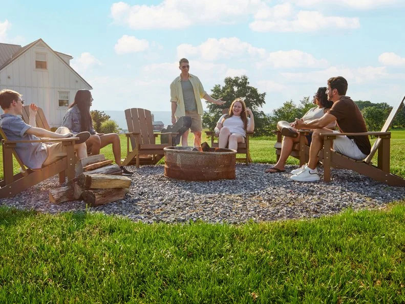 People sitting and standing around a fire pit in a back yard
