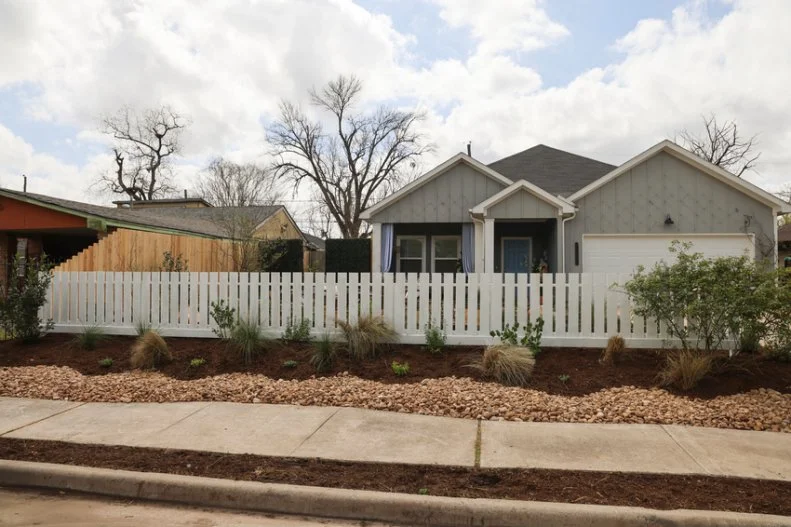 well-placed mulch, plant life, river rocks and a white picket fence