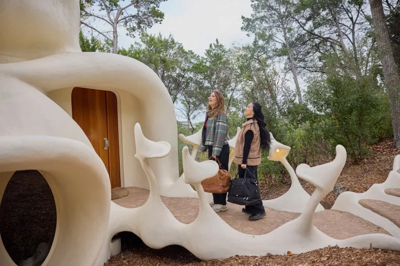 Host Sherry Cola and D’Arcy Carden walk to the entry of the Bloomhouse, as seen on Wild Vacation Rentals, Season 1.