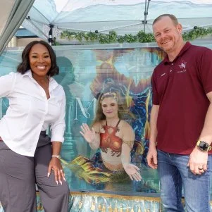 Host Noel Collier and Nate posing and smiling with Megan in mermaid costume inside tank, as seen on Extreme Buyers Club, Season 1.