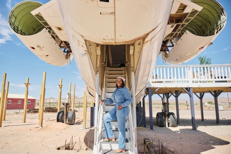 Host Noel Collier poses for a photos in front of the finished airplane house, as seen on Extreme Buyers Club, Season 1.