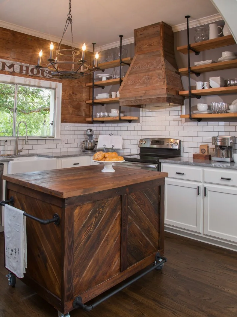 Hosts Chip and Joanna Gaines expanded the entryway to the kitchen by cutting a wide archway, which creates a better flow between the kitchen and dining room. They painted one wall a neutral gray and for the other, they brought in shiplap to match the rest of the house. A white subway tile backsplash and Super White Quartzite countertops add a modern element. There are new cabinets, a wood vent hood, stainless appliances and an under-mounted sink. Modern shelving made from plumbing pipes and wood planks offer additional open storage, and a custom kitchen island made from vintage wood contributes style and utility in the kitchen, as seen on Fixer Upper. (afters)