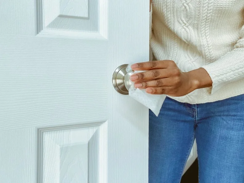 Close-up of unrecognizable woman cleaning doorknob on interior door with disinfectant wipe