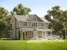 A water sprinkler watering a lawn in front of a house in the daytime