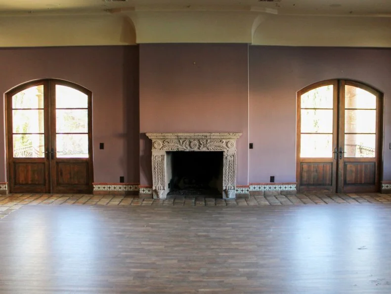 Rose room, empty room, arched doors, fireplace, wood flooring, interior wide shot, pre-makeover, as seen on Bachelor Mansion Takeover, Season 1.