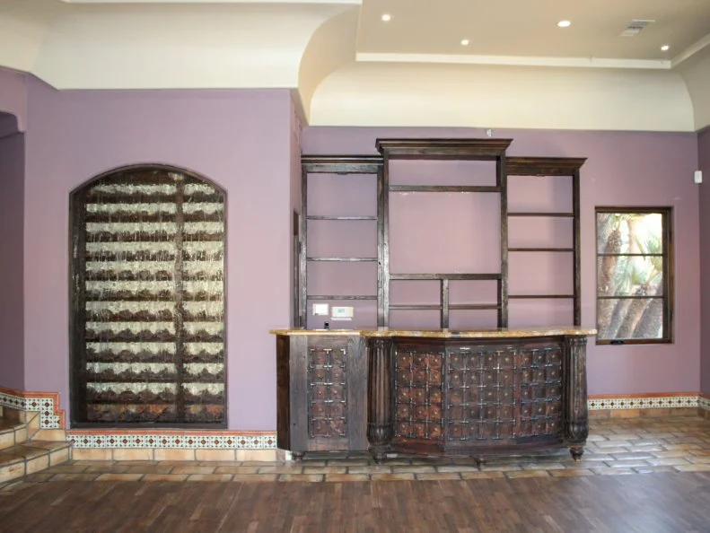 Bar counter, shelving wall, arched window, interior wide shot, pre-makeover, as seen on Bachelor Mansion Takeover, Season 1.