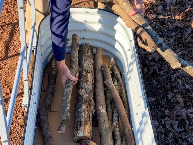 Person placing logs inside raised garden bed for layering