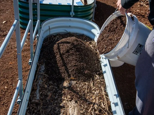 Pouring soil into raised garden bed over wood base layer