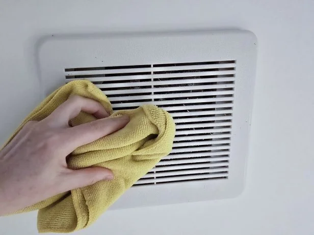 Person wipes dust from bathroom ventilation cover with a microfiber cloth.