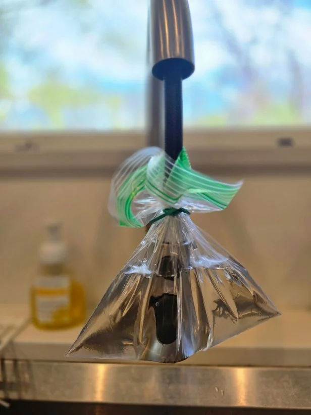 A baggie wrapped around a kitchen sink faucet.