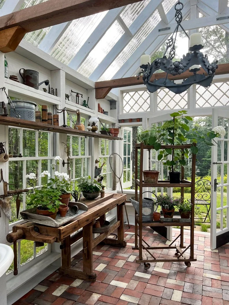 Sunlit greenhouse interior with wooden bench, potted plants, tools