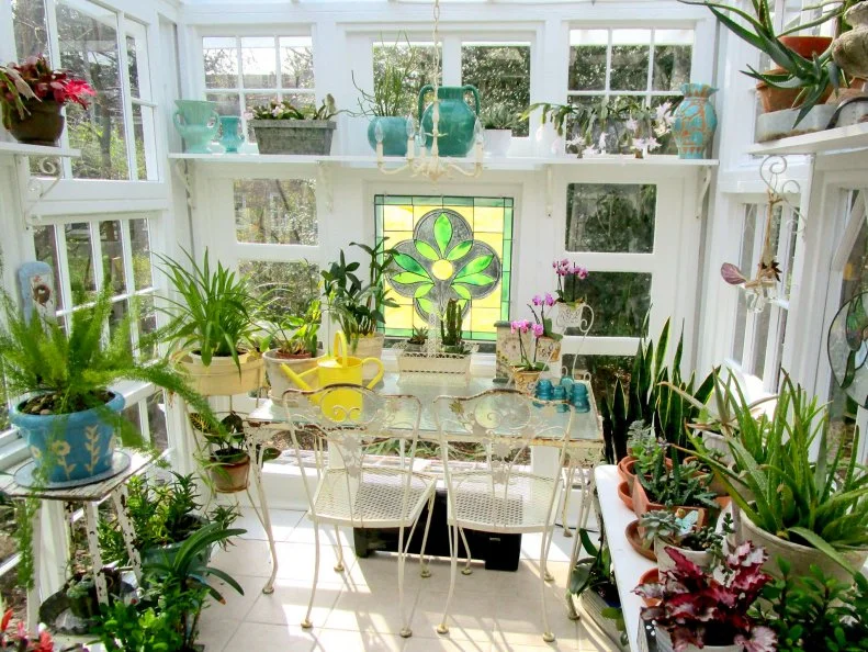 Bright sunroom filled with potted plants and vintage white furniture