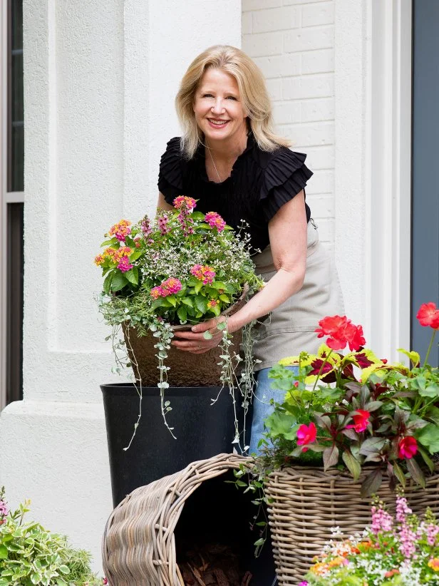 Woman arranging colorful flowering planters on elegant front porch