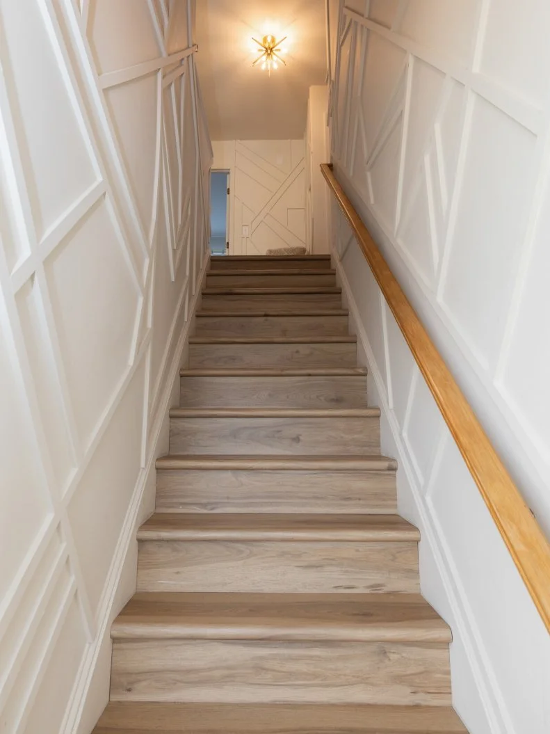 After of Team Sarah Baeumler’s living room renovation that included custom wall detailing for the staircase and second floor landing, as seen on Battle on the Beach, Season 5.
