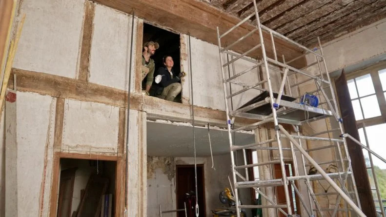 Candid of Ian Figuera and Daphne Reckert looking/peeking out from the mezzanine at their work in the Library so far, after exposing a hole in the wall, as seen on Castle Impossible, Season 2.