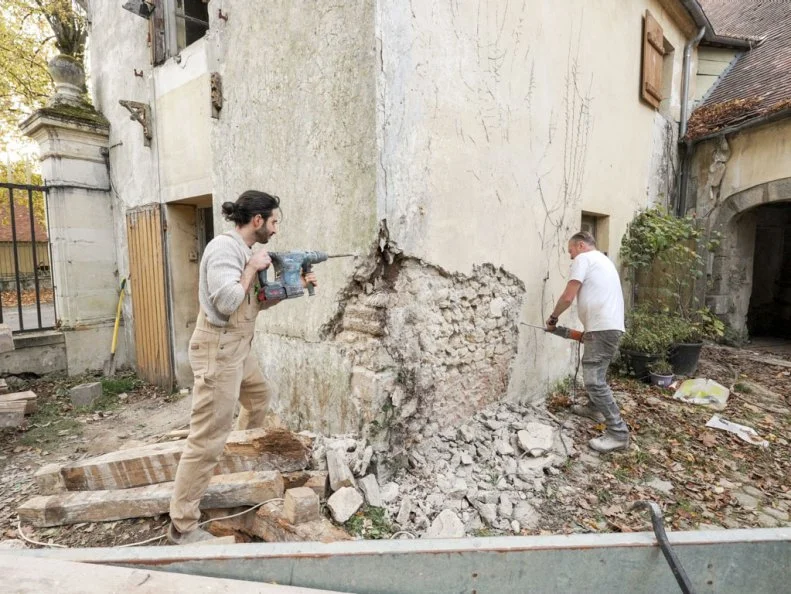 Tony and Ian Figueira chipping away at the exterior coating of the gatehouse to expose stone, as seen on Castle Impossible, Season 2.