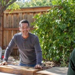 Exterior shot of Jon Knight and Anthony at the work table working on custom shelves during the renovation, as seen on Crashers, Season 1.