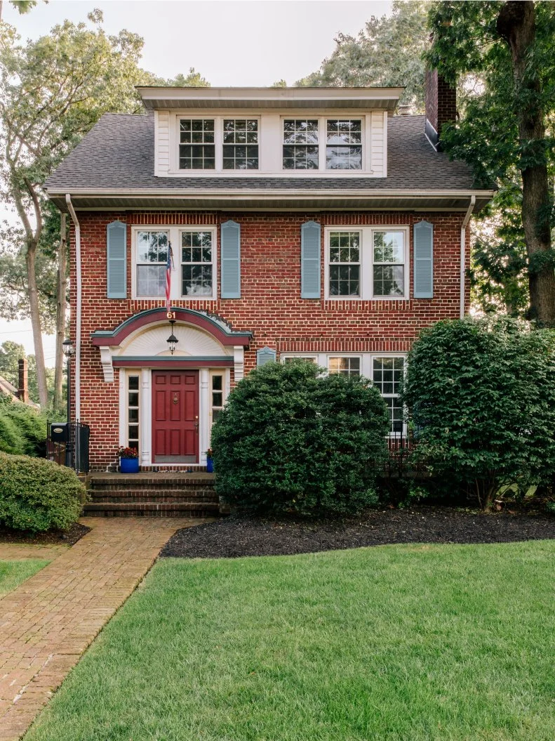 HGTV Magazine features this Northeastern brick-faced home with a dark red door and light blue shutters.