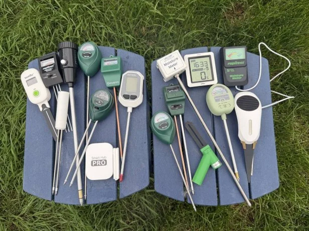 Fifteen soil moisture meters arranged together on a navy blue outdoor side table siting atop green grass
