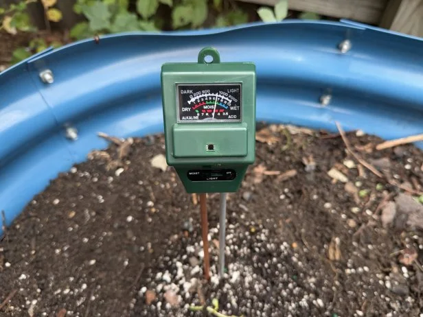 Sonkir Soil Moisture Meter probed in outdoor potting soil in a blue raised garden bed