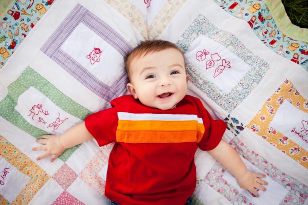 Color image of a smiling, six-month-old baby boy lying on his back on a handmade quilt outdoors.