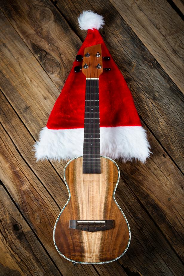 A ukulele with a Christmas hat against a wooden background.