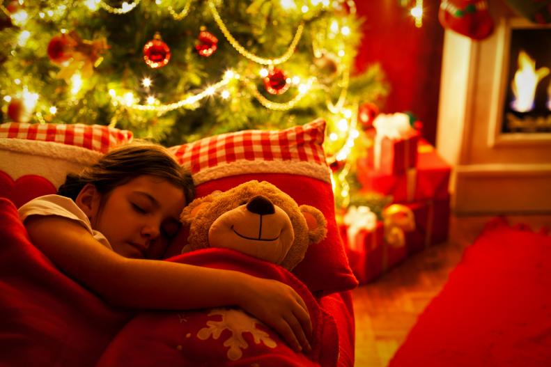 Beautiful little girl with their toy teddy bear sleeping in front of the fireplace and Christmas tree