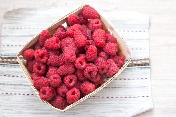 Fresh raspberries in a wicker basket on a village tablecloth, top view. Healthy helpful food.