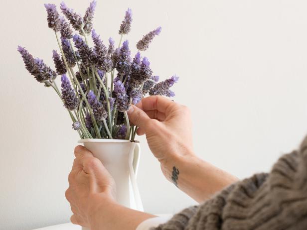 Cropped view of woman's hands arranging lavender in small white jug (selective focus)