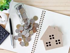 Business, finance, savings, property ladder or mortgage loan concept : Flat lay or top view of wood house model and coins scattered from glass jar on open blank notebook paper