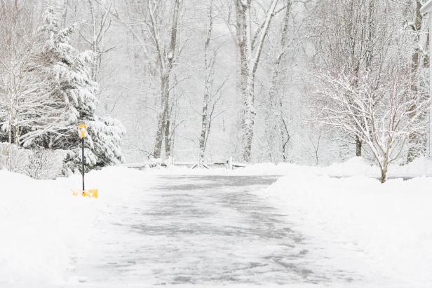 Yellow snow shovel, placed along the side of a driveway, that has been freshly shoveled. Taken in winter.