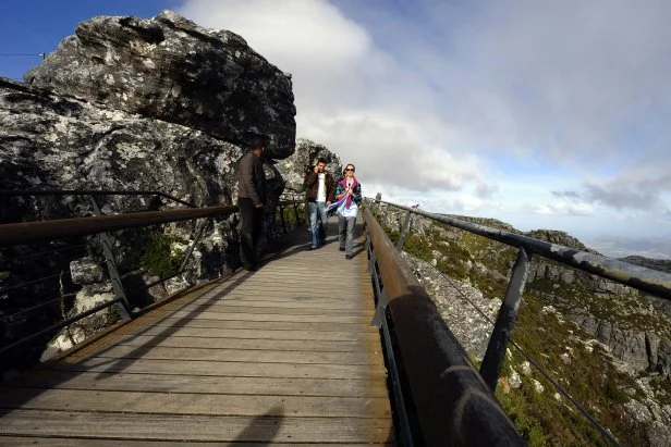Tourists walk on a bridge on the south side of Table Mountain at the arrival station of the Table mountain cableway on May 7, 2010 in Cape Town, South Africa. Table Mountain cableway has been running for over 80 years and the cars feature a floor which can rotate while ascending to give passengers a 360 degree panoramic views.  AFP PHOTO/GIANLUIGI GUERCIA (Photo credit should read GIANLUIGI GUERCIA/AFP via Getty Images)