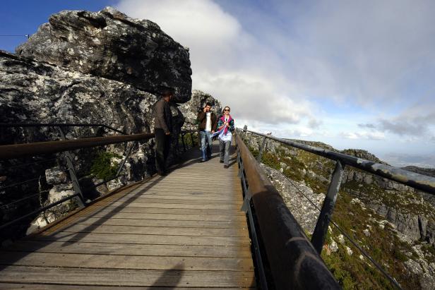 Tourists walk on a bridge on the south side of Table Mountain at the arrival station of the Table mountain cableway on May 7, 2010 in Cape Town, South Africa. Table Mountain cableway has been running for over 80 years and the cars feature a floor which can rotate while ascending to give passengers a 360 degree panoramic views.  AFP PHOTO/GIANLUIGI GUERCIA (Photo credit should read GIANLUIGI GUERCIA/AFP via Getty Images)