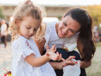 Woman smiling when looking her daughter removing chocolate stains from a dress