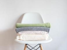 towels and soft fleecy cloths lie neatly folded on a chair against a white background. Clean house, order in the house, minimalism.