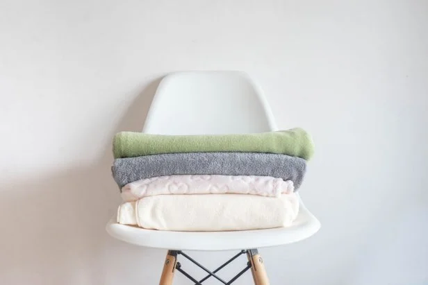 towels and soft fleecy cloths lie neatly folded on a chair against a white background. Clean house, order in the house, minimalism.