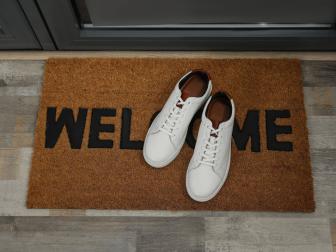 Pair of stylish white sneakers on doormat near entrance, above view