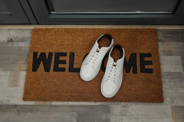 Pair of stylish white sneakers on doormat near entrance, above view