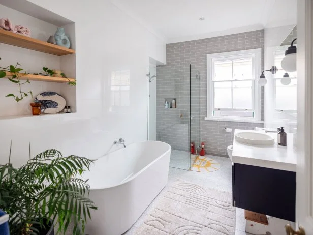 A bright bathroom featuring a sleek freestanding tub, a large shower area, big windows, greenery, and simple decor, creating a calming and refreshing atmosphere.
