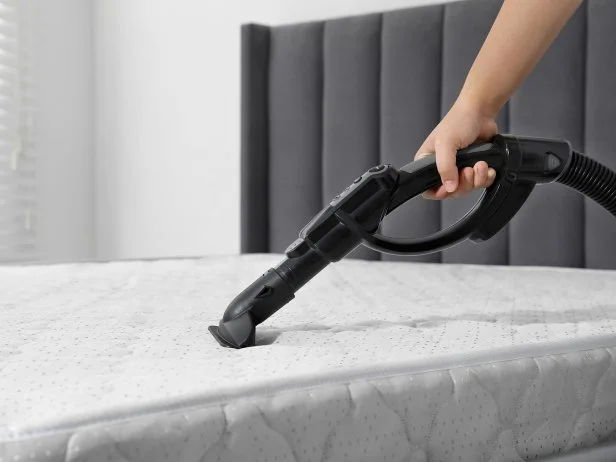 Woman disinfecting mattress with vacuum cleaner indoors, closeup. Space for text