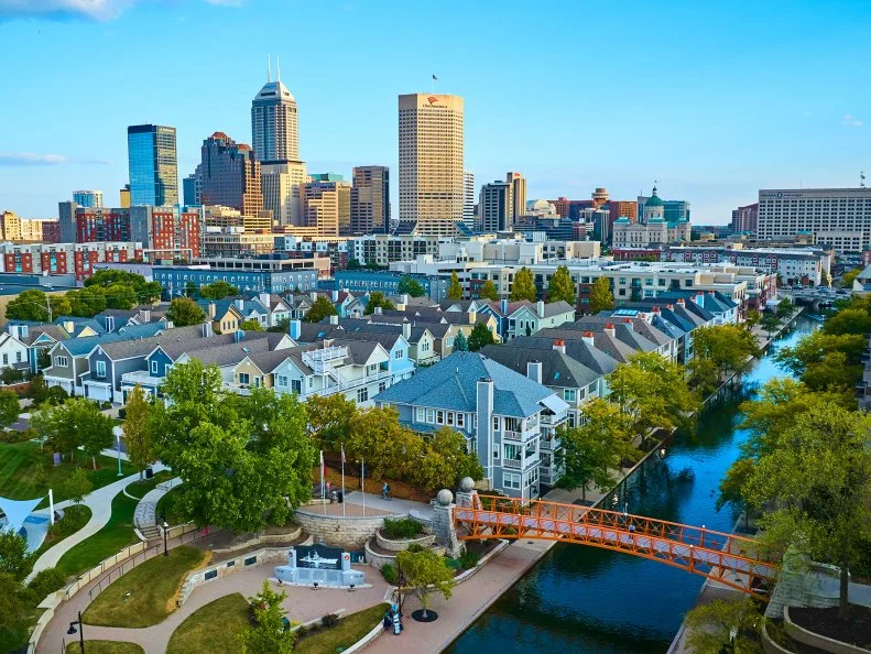Aerial view of modern and historic skyline in Indianapolis during golden hour, showcasing a vibrant residential area with a canal and walking bridge