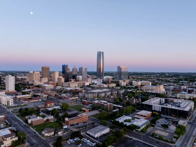 Stunning aerial sunrise view of Oklahoma City skyline with Devon Energy Center standing tall and visible moon, highlighting urban landscape and architectural marvels.