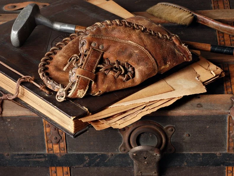 Vintage still life with antique baseball glove, golf club and scrapbook on rustic old steamer trunk.