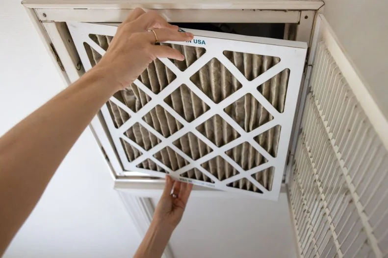 Dirty air filter being removed from a home air intake vent by a homeowner.