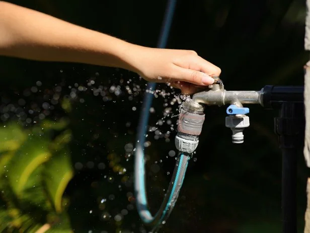 Hand turning outdoor water tap connected to garden hose