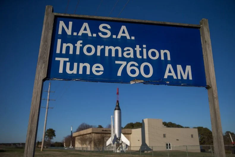A "NASA Information" sign stands near National Aeronautics and Space Administration's (NASA) Wallops Space Facility visitor center in Wallops Island, Virginia, U.S., on Monday, March 31, 2014. Alone among space companies, Orbital Sciences Corp. launches rockets from NASA's Wallops Space Facility on the eastern shore of its home state of Virginia. Orbital is soaring on plans to combine with Alliant Techsystems Inc. (ATK)'s aerospace and defense businesses, tripling revenue and uniting two longtime launch partners. Alliant helps power the Antares rocket, key to Orbital's growth in the estimated $7 billion market for building and launching midsized satellites and spacecraft. Photographer: Andrew Harrer/Bloomberg via Getty Images