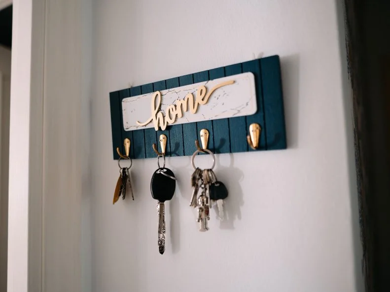 A wall-mounted "home" key rack with three sets of keys hanging from its gold hooks