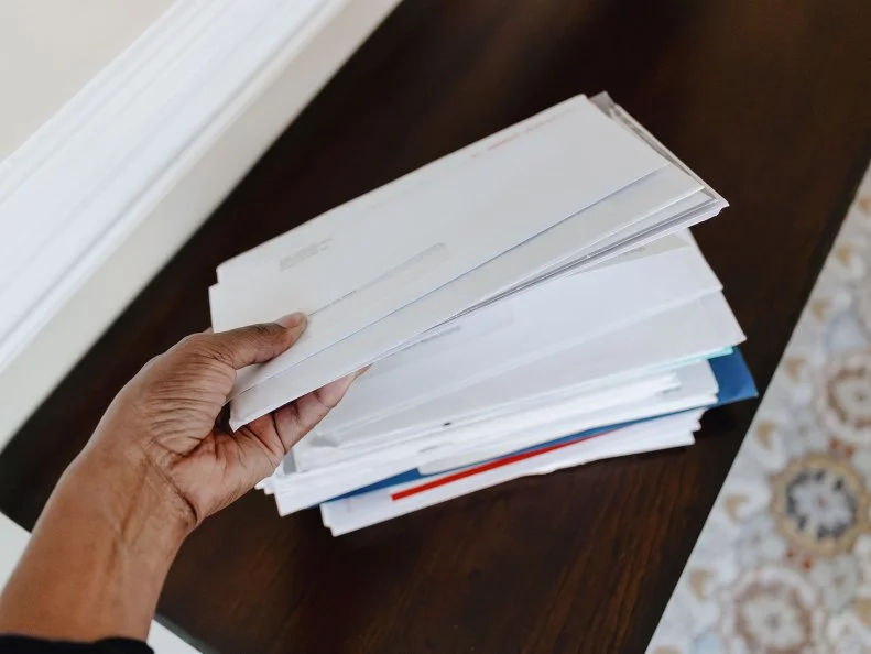 A hand sorting through a stack of mail and envelopes on a wooden table.